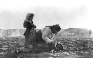 Armenian woman kneeling beside dead child in field.